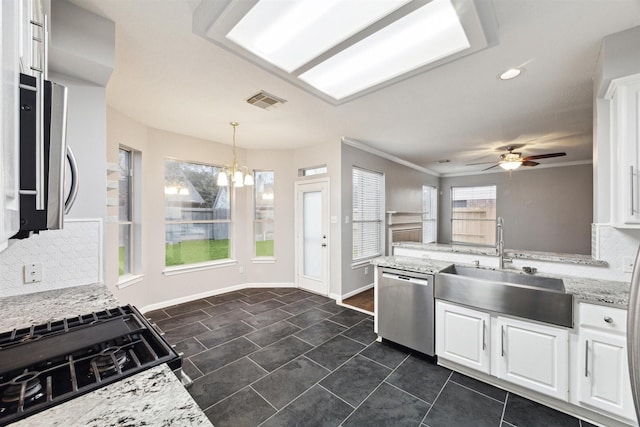 kitchen with sink, light stone countertops, white cabinets, decorative light fixtures, and stainless steel dishwasher