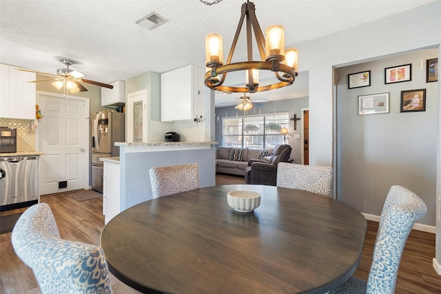 dining space featuring ceiling fan with notable chandelier, a textured ceiling, and dark hardwood / wood-style floors