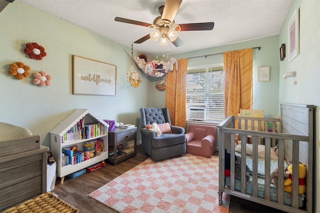 bedroom with ceiling fan, a nursery area, a textured ceiling, and hardwood / wood-style flooring