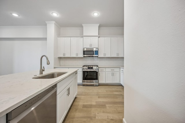 kitchen featuring light stone countertops, white cabinetry, stainless steel appliances, sink, and backsplash