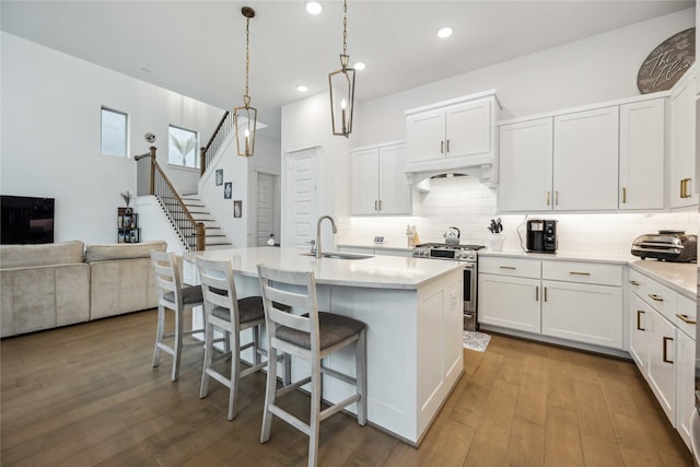 kitchen with a kitchen island with sink, sink, stainless steel range with gas stovetop, and white cabinets