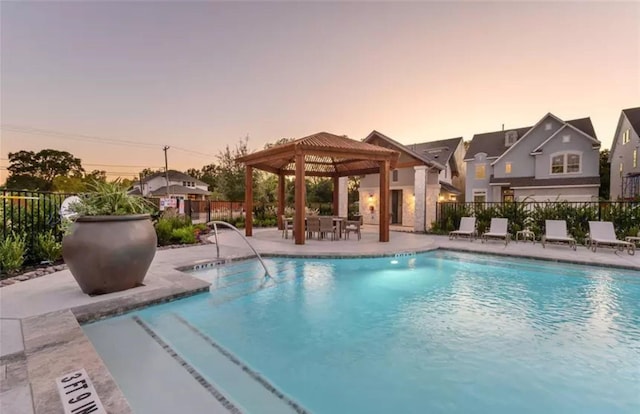 pool at dusk featuring a patio area, fence, a gazebo, and a community pool