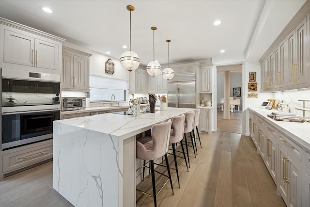 kitchen featuring a spacious island, appliances with stainless steel finishes, hanging light fixtures, light wood-type flooring, and a breakfast bar