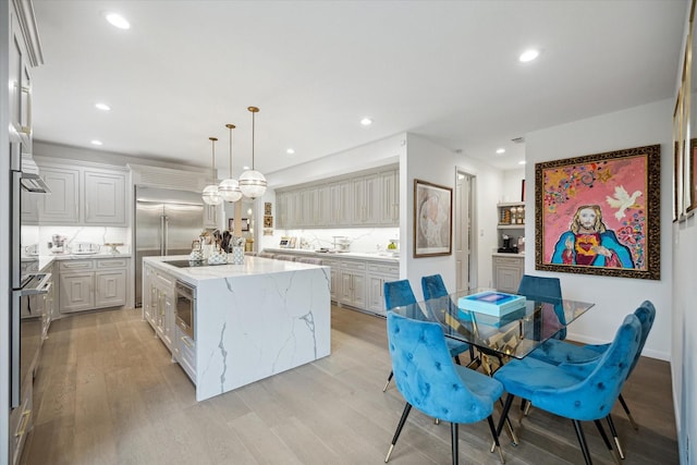 kitchen featuring light wood-type flooring, decorative light fixtures, a center island, and light stone countertops