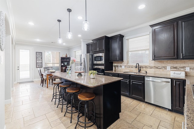 kitchen featuring appliances with stainless steel finishes, a kitchen island, a kitchen bar, sink, and hanging light fixtures