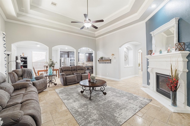 living room featuring a towering ceiling, a raised ceiling, crown molding, and ceiling fan