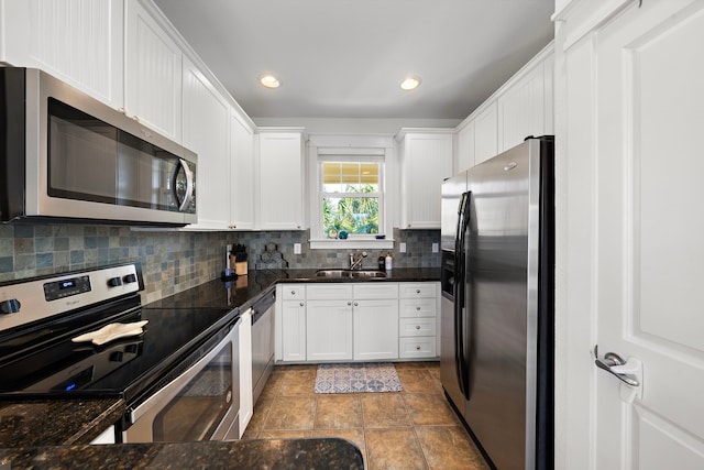 kitchen with appliances with stainless steel finishes, sink, tasteful backsplash, white cabinetry, and dark stone countertops