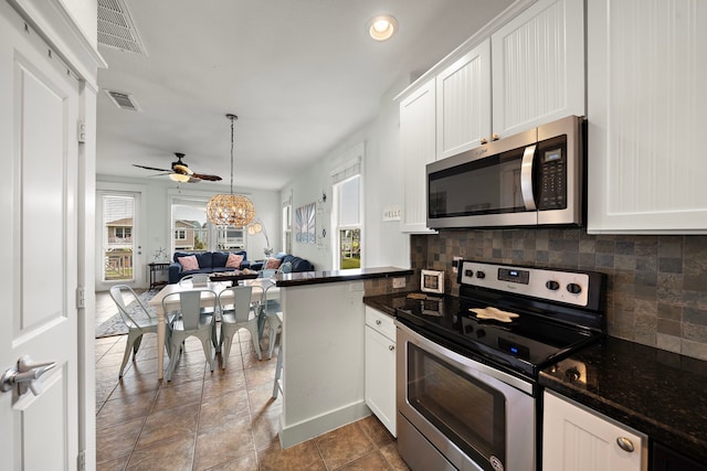 kitchen with kitchen peninsula, appliances with stainless steel finishes, white cabinets, dark stone countertops, and decorative backsplash