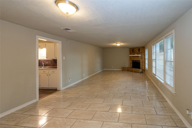 unfurnished living room with a brick fireplace, a textured ceiling, and light tile patterned flooring