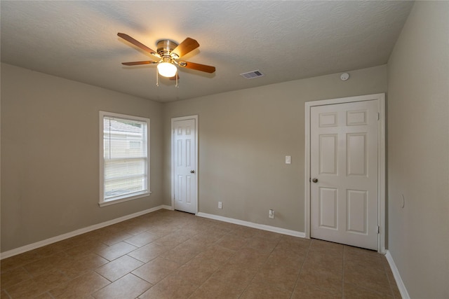 empty room with ceiling fan, a textured ceiling, and light tile patterned floors