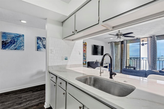 kitchen with sink, backsplash, light stone counters, and dark wood-type flooring