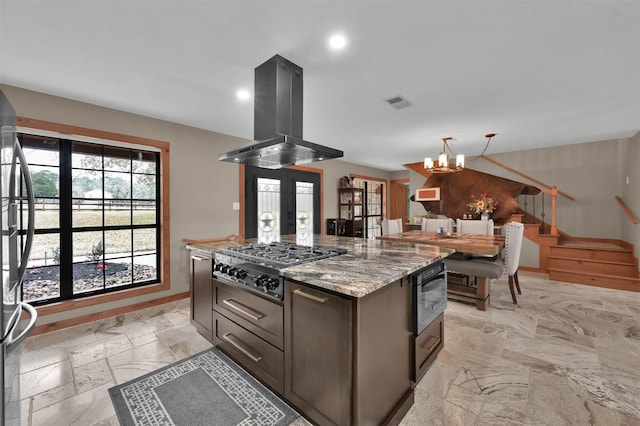 kitchen with stainless steel appliances, light stone counters, island range hood, french doors, and a chandelier