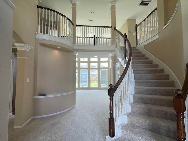 staircase featuring a towering ceiling, carpet flooring, and ornate columns