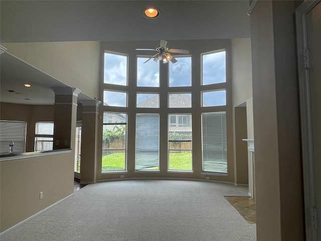 unfurnished room with ceiling fan, light colored carpet, a high ceiling, and ornate columns