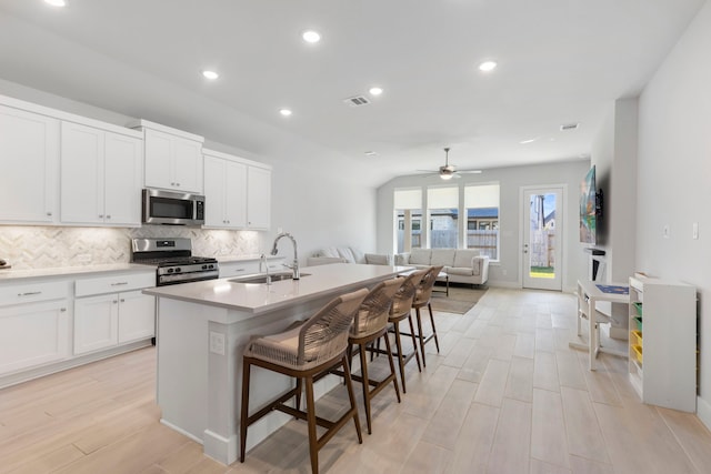 kitchen with sink, a kitchen breakfast bar, stainless steel appliances, an island with sink, and white cabinets