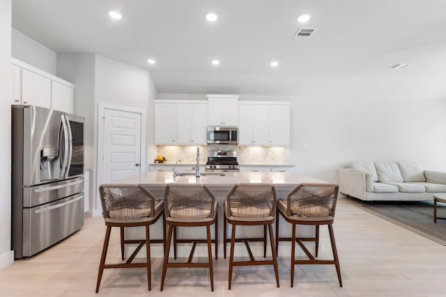 kitchen with appliances with stainless steel finishes, a breakfast bar, white cabinetry, sink, and a center island with sink