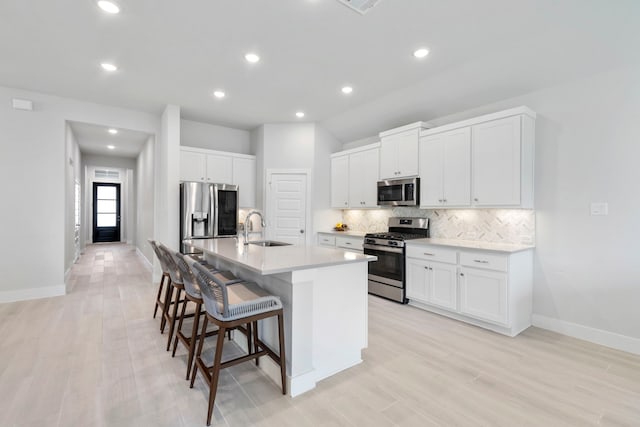 kitchen with sink, a breakfast bar area, stainless steel appliances, a kitchen island with sink, and white cabinets