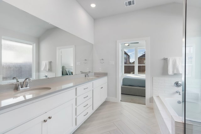 bathroom featuring tiled tub, vanity, vaulted ceiling, and a wealth of natural light