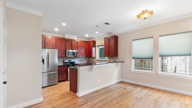 kitchen with appliances with stainless steel finishes, a kitchen breakfast bar, tasteful backsplash, ornamental molding, and kitchen peninsula