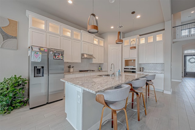 kitchen featuring sink, appliances with stainless steel finishes, light stone counters, white cabinets, and a center island with sink