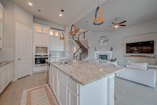 kitchen featuring sink, appliances with stainless steel finishes, a kitchen island with sink, hanging light fixtures, and white cabinets