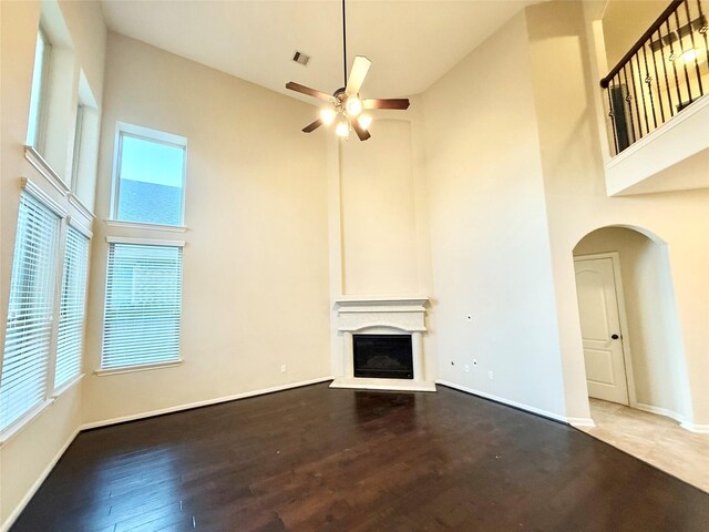 unfurnished living room featuring wood-type flooring, plenty of natural light, a towering ceiling, and ceiling fan