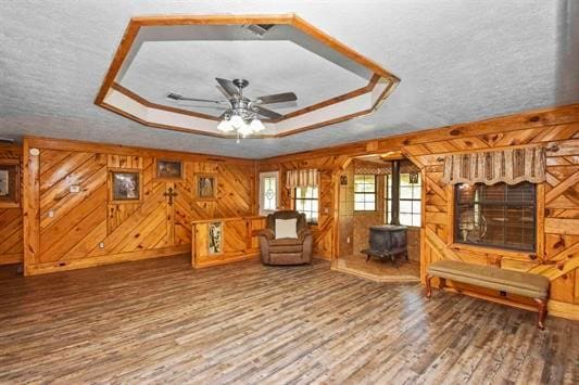 living area featuring a raised ceiling, a wood stove, hardwood / wood-style floors, a textured ceiling, and wood walls