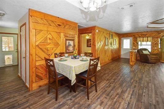 dining space featuring dark wood-type flooring, a notable chandelier, and wooden walls