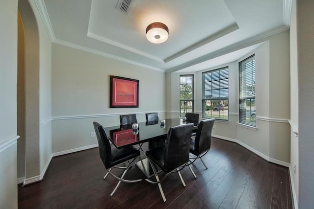 dining area with dark wood-type flooring, ornamental molding, and a tray ceiling