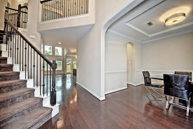 foyer with dark wood-type flooring, ornamental molding, and a high ceiling