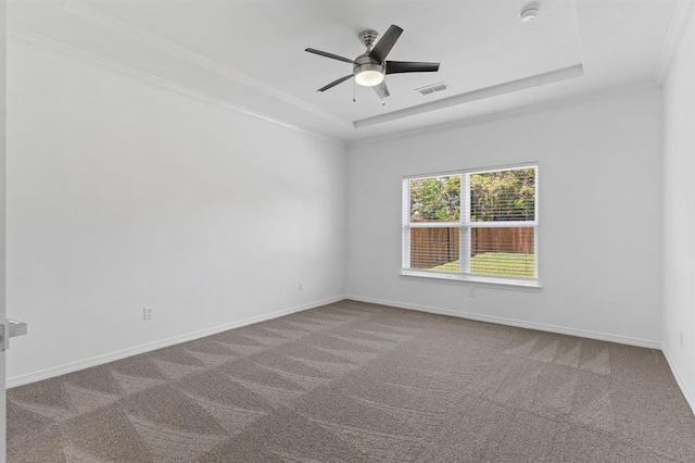 empty room with a tray ceiling, ornamental molding, ceiling fan, and carpet