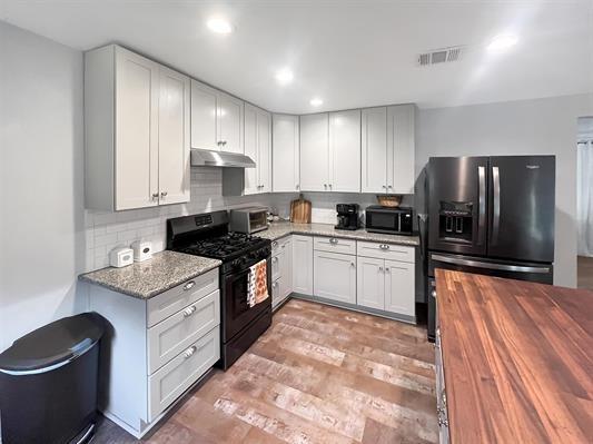 kitchen featuring white cabinets, stainless steel refrigerator with ice dispenser, dark stone countertops, decorative backsplash, and black gas stove