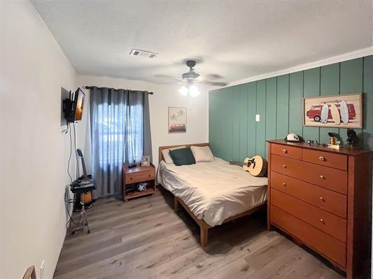 bedroom featuring light wood-type flooring, wooden walls, and ceiling fan