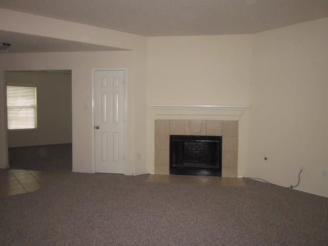 unfurnished living room featuring carpet floors and a tiled fireplace