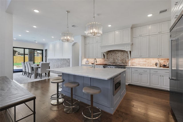 kitchen featuring white cabinetry, decorative light fixtures, dark hardwood / wood-style flooring, and a kitchen island with sink