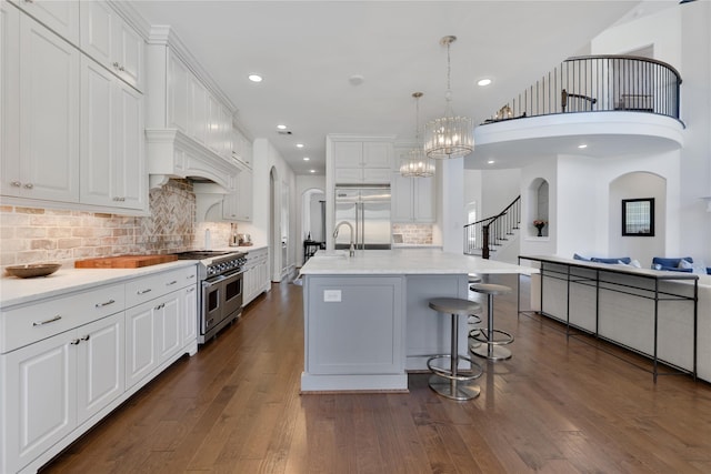 kitchen with high quality appliances, white cabinetry, a center island with sink, and decorative backsplash