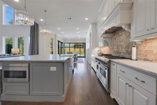 kitchen featuring backsplash, custom range hood, white cabinets, and range with two ovens