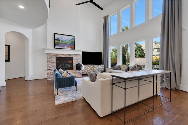 living room with a towering ceiling, dark hardwood / wood-style floors, and a brick fireplace