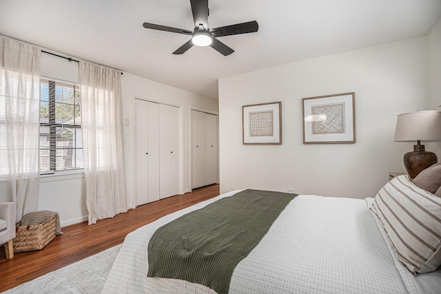 bedroom with hardwood / wood-style flooring, two closets, and ceiling fan