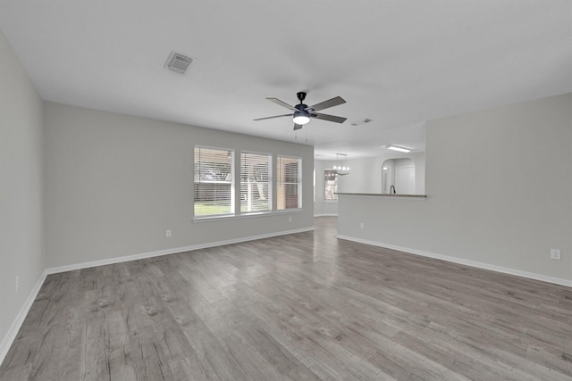 unfurnished living room featuring ceiling fan with notable chandelier and light hardwood / wood-style flooring