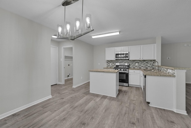 kitchen featuring appliances with stainless steel finishes, decorative light fixtures, white cabinetry, sink, and light wood-type flooring