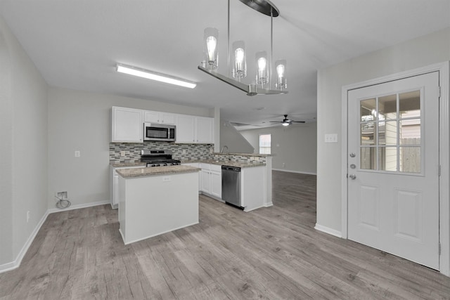 kitchen with appliances with stainless steel finishes, decorative backsplash, white cabinets, decorative light fixtures, and kitchen peninsula