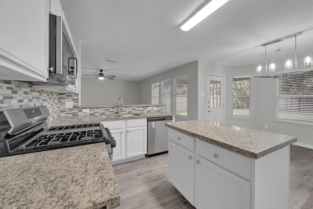 kitchen featuring white cabinetry, sink, a kitchen island, decorative light fixtures, and stainless steel appliances