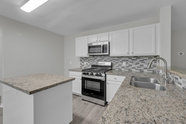 kitchen with appliances with stainless steel finishes, white cabinetry, sink, light hardwood / wood-style flooring, and backsplash