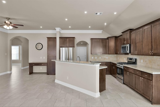 kitchen featuring light stone counters, a center island with sink, dark brown cabinetry, and appliances with stainless steel finishes