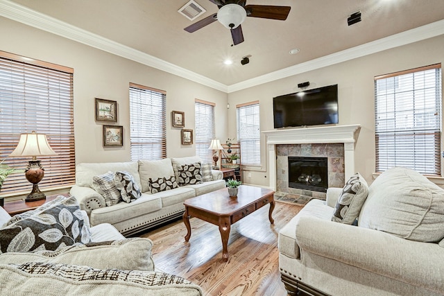 living room with light hardwood / wood-style flooring, crown molding, a tiled fireplace, and a healthy amount of sunlight