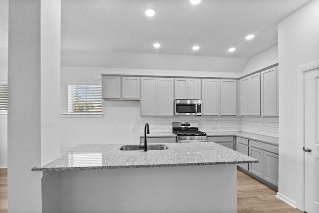 kitchen featuring light stone countertops, appliances with stainless steel finishes, decorative backsplash, sink, and light hardwood / wood-style flooring