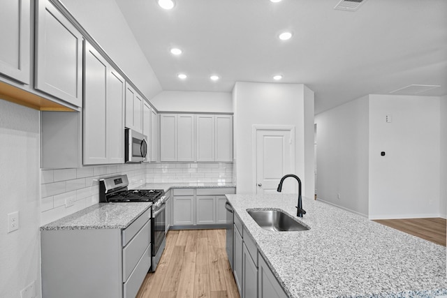 kitchen with sink, stainless steel appliances, light stone counters, and gray cabinets