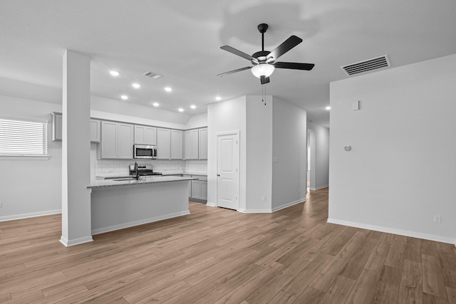 kitchen featuring sink, backsplash, light wood-type flooring, and light stone countertops