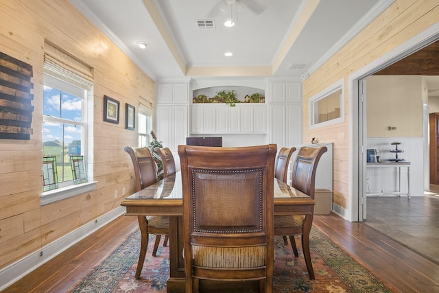 dining room featuring dark hardwood / wood-style flooring, ornamental molding, a raised ceiling, and wood walls